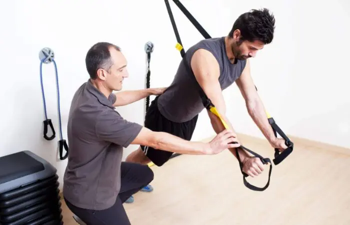 A man is holding onto a trx rope while another man watches.
