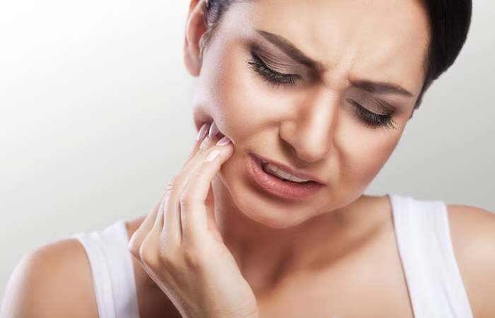 A woman holding her face in pain with one hand and the other hand on her cheek.