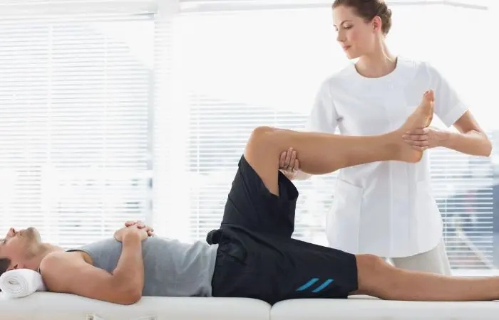 A man is stretching on the couch while another person watches.