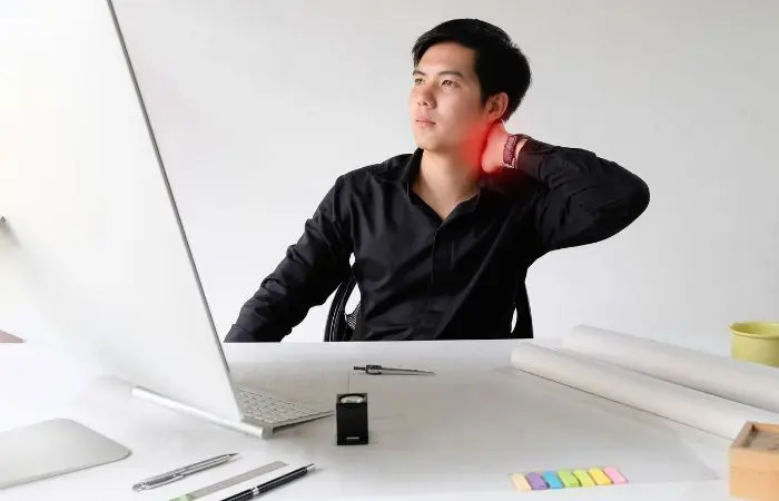 A man sitting at his desk with one hand on the back of his head.